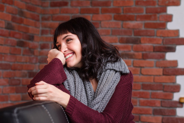 迷人的害羞的年轻女子坐在皮沙发和大笑图片下载