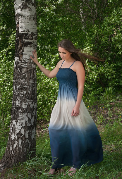 穿着蓝色裙子的美丽年轻女子站在一棵桦树旁图片下载
