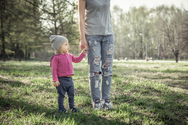 孩子和妈妈手牵着手在夏天公园的草地上散步。主题是儿童。照片上不认识的母亲。归属感和关怀的概念。图片下载