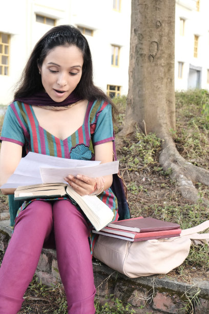 惊讶的印度女性在树下研究一封信。图片下载