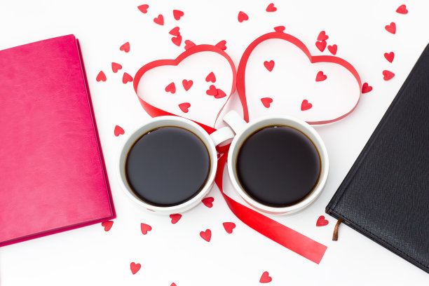 两个咖啡杯用红丝带系成心形，两个日记本放在白色背景上。图片下载