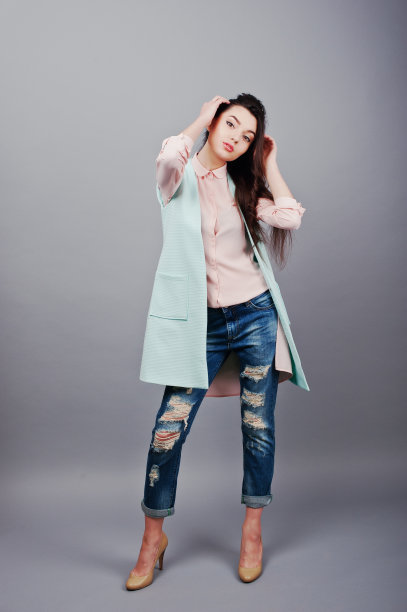 全身肖像年轻的黑发女孩穿着粉红色衬衫，绿松石夹克，破洞牛仔裤和奶油色鞋子。时尚工作室拍摄图片下载