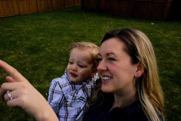 母亲抱着蹒跚学步的儿子穿过公共草地公园图片下载