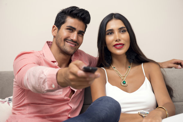 年轻的中东夫妇在沙发上看电视图片下载