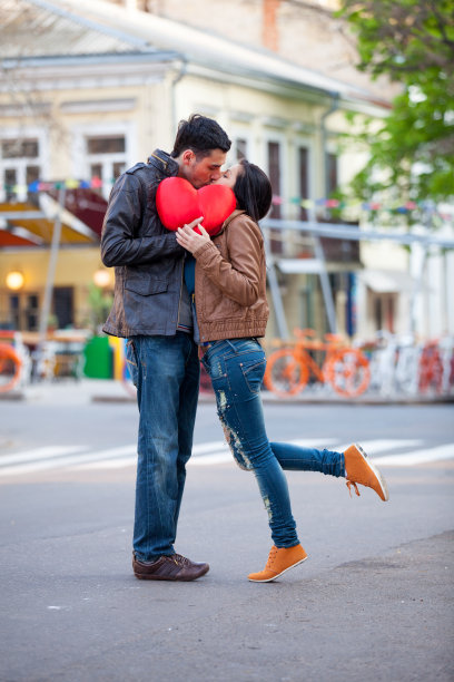 这对可爱的情侣抱着心形枕头，在美妙的街道背景上接吻图片下载