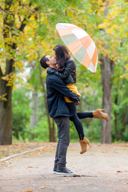 在美丽的秋天公园背景下，可爱的情侣在伞下拥抱和亲吻的照片图片下载
