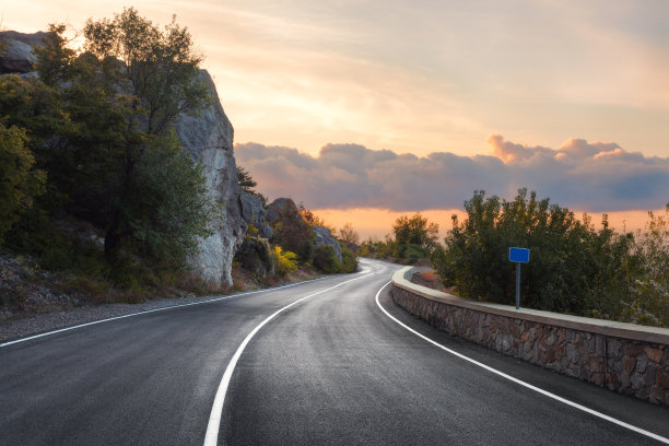 沥青道路。风景与岩石，阳光灿烂的天空与云彩和美丽的山路与完美的柏油日出在夏天。古董塑身。旅游的背景。欧洲山区的高速公路图片下载