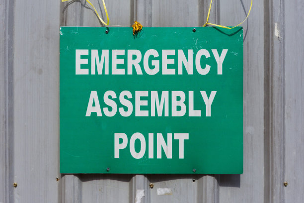 绿色应急集合点标志安装在建筑工地的金属围栏上。图片下载