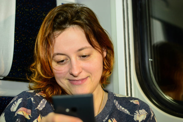 一个红卷发的女人在火车上使用智能手机图片下载