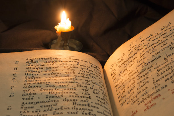 打开书，烛光柔和的光线倾泻在文字上。开卷阅读教育读者。在黑色背景上阅读古代圣经文本。俄罗斯的圣经。古斯拉夫语文本和字母图片下载