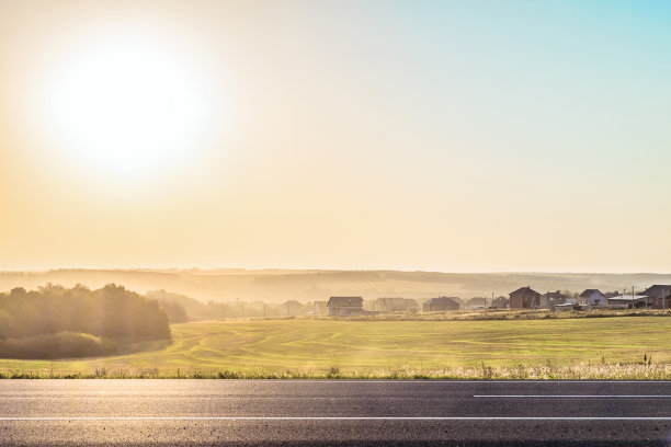 路边的乡村景观在夕阳的照射下背光。从一个阳光灿烂的俄罗斯村庄的道路上看。阳光明媚的地平线上有薄雾。别尔地区。图片下载