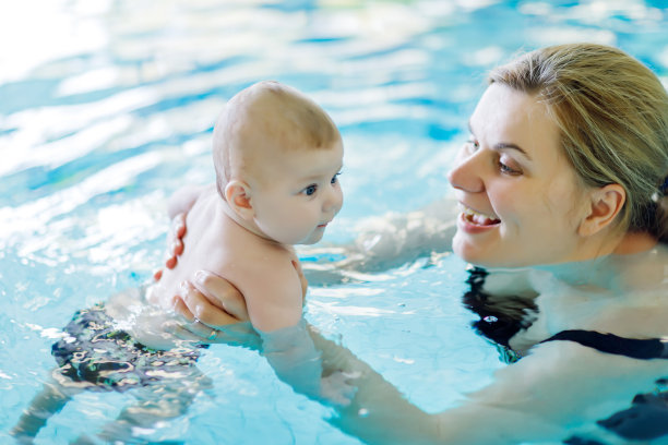 快乐的中年母亲和可爱的宝宝在游泳池游泳。素材图片