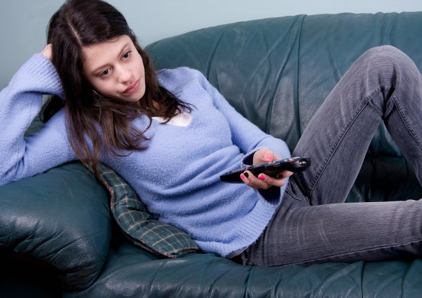 一个无聊的女孩坐在沙发上用遥控器玩电子游戏图片下载
