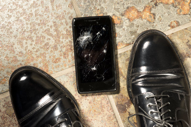 在工作鞋旁边的地板上摔碎的黑色智能手机图片下载