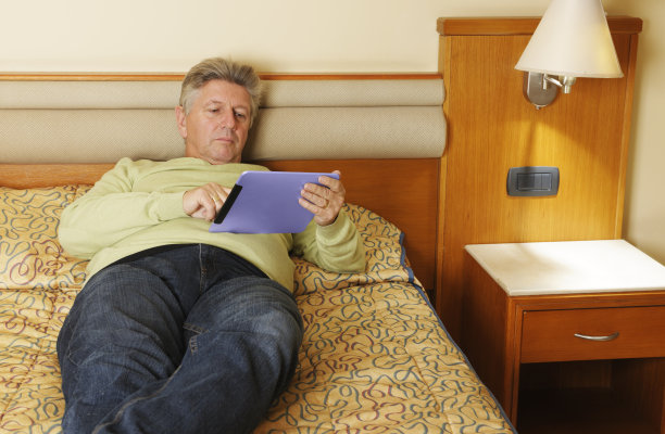 白种人在床上放松时使用数字平板电脑。图片下载