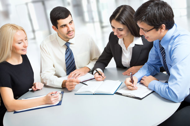 四个商务人士围着桌子对着一本书微笑图片下载