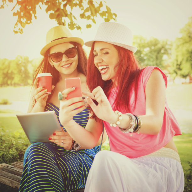 两个红头发的年轻女人在户外玩智能手机和平板电脑图片下载