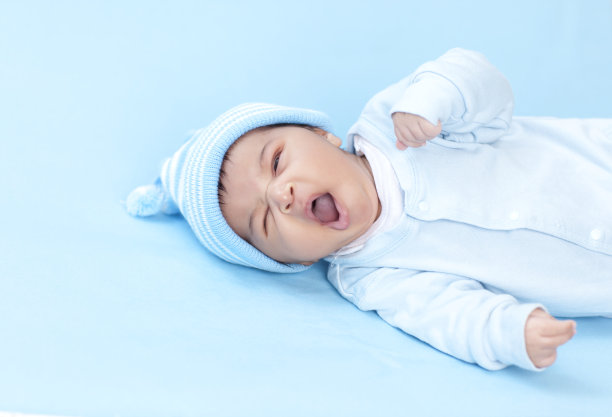 在蓝色背景上打哈欠的新生儿。图片下载