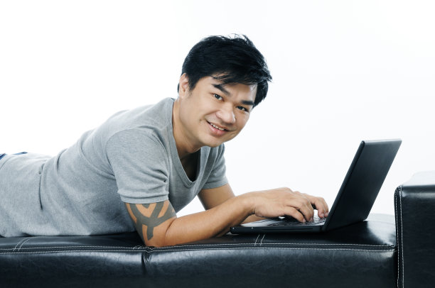 快乐的年轻人躺在沙发上使用笔记本电脑图片下载