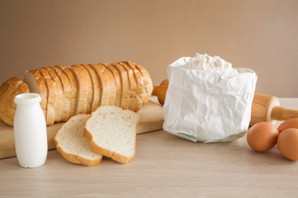 新鲜的切片面包和面粉，牛奶和鸡蛋放在厨房的木板上。健康的饮食和生活方式。图片下载