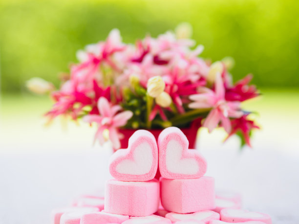 木盘上的心形棉花糖和背景上的花朵的特写图片下载