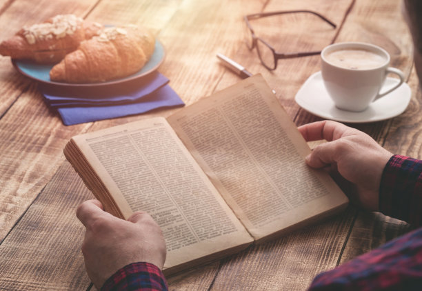坐在木桌边吃早餐和看书的人图片下载