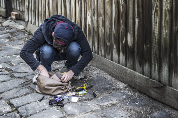 一个男小偷正在检查一个被偷的手提包图片下载