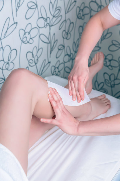 美容师的手做脱毛的女人的腿与蜡条图片下载