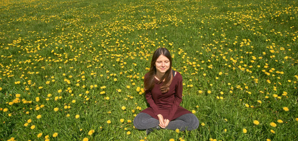 美丽的微笑的年轻女子放松在草地上的蒲公英在春天的阳光。正面视图与copyspace。图片下载