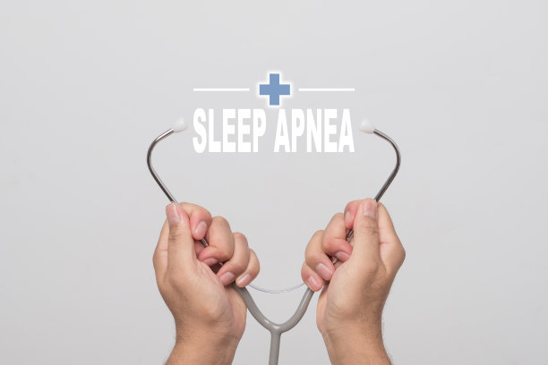 双手拿着听诊器，灰色背景上写着“睡眠呼吸暂停”。健康的概念。图片下载