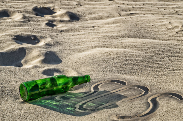 一个绿色的空瓶子躺在沙滩上图片下载