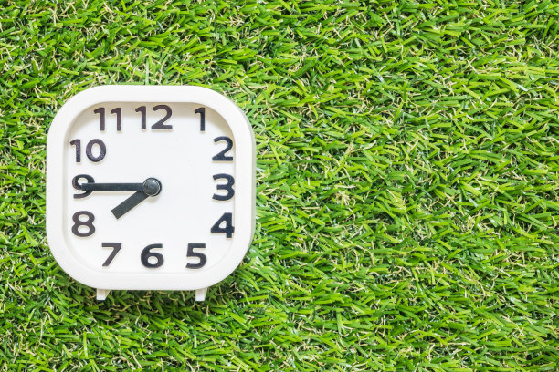 特写白色时钟装饰显示八点一刻或早上7:45在绿色人造草地板纹理背景与复制空间图片下载