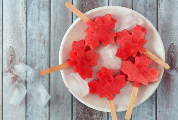 白色盘子上放着加拿大枫叶西瓜，衬着木头图片下载