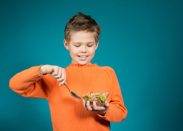 可爱的男孩吃麦片孤立在蓝色背景。健康食品。图片下载