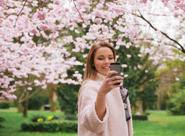 年轻女子在春天的花园拍照图片下载