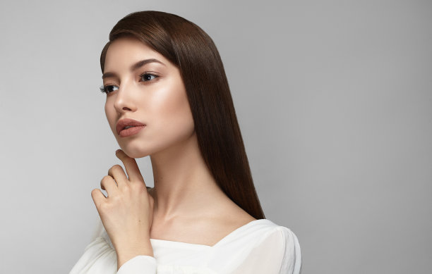 美丽的女人的脸。美丽性感的年轻女性肖像与完美的化妆，柔软新鲜健康的皮肤和厚厚的黑色长睫毛。灰色背景下的迷人女孩。高分辨率图片下载