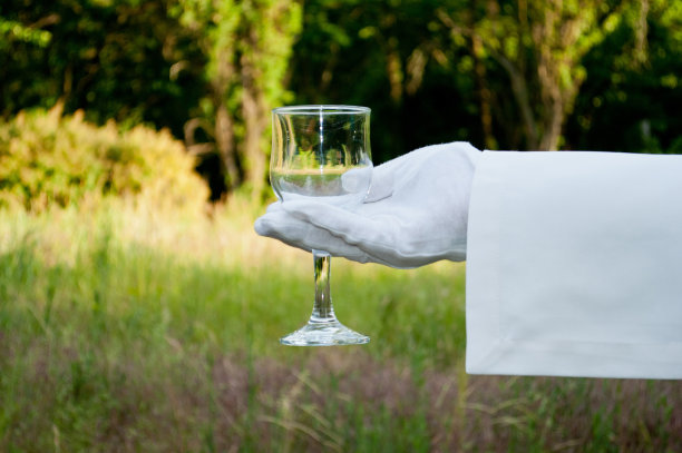 在大自然中，一个戴着白手套的服务员的手拿着一个玻璃杯图片下载