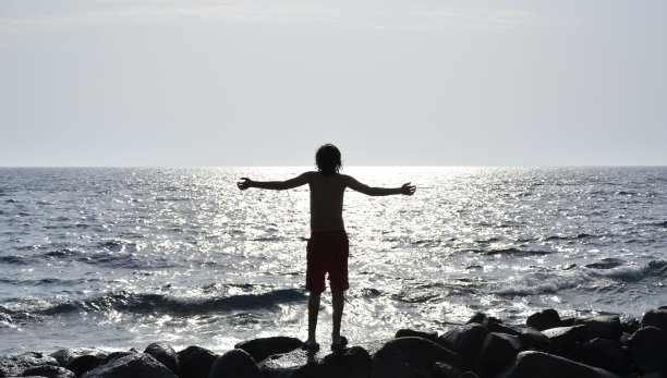 男孩站在海滩上的岩石上图片下载