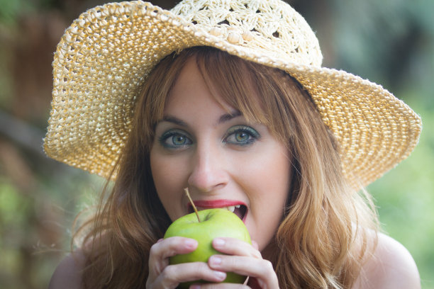 金发碧眼，戴着帽子，咬着一个绿色的苹果。图片下载