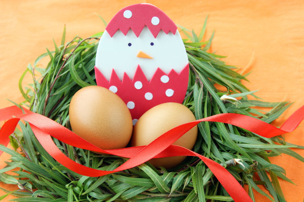 复活节装饰:黄色的鸡蛋和手工孵出的小鸡蛋壳在绿草枝窝在橙色的背景图片下载