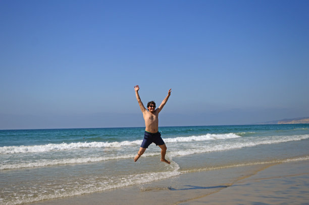 快乐的游客男子在海滩上跳高，享受在圣地亚哥，加利福尼亚，美国的假期图片下载