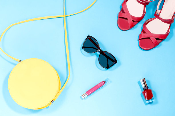 黄色的圆钱包，红色的指甲油，红色的口红，红色的凉鞋，淡蓝色背景的太阳镜图片下载