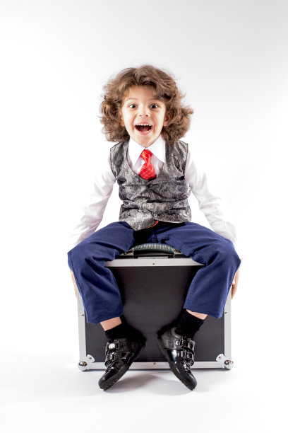 可爱的卷发小男孩坐在黑色的公文包上图片下载