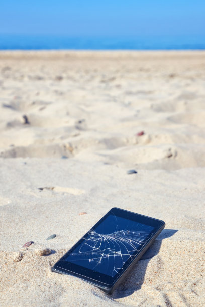 手机和破碎的屏幕在沙滩上的沙子。图片下载