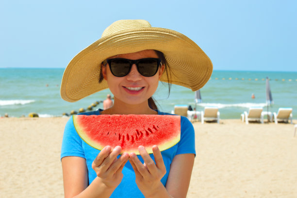 美丽的年轻女子在海滩上拿着西瓜图片下载