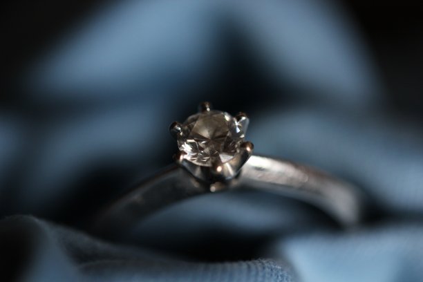 订婚戒指戴在蓝色的纺织品上图片下载