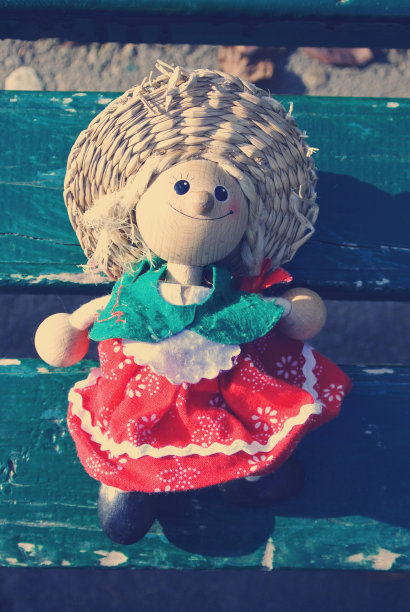 小娃娃穿着五颜六色的衣服坐在绿色的长凳上;复古的风格图片下载