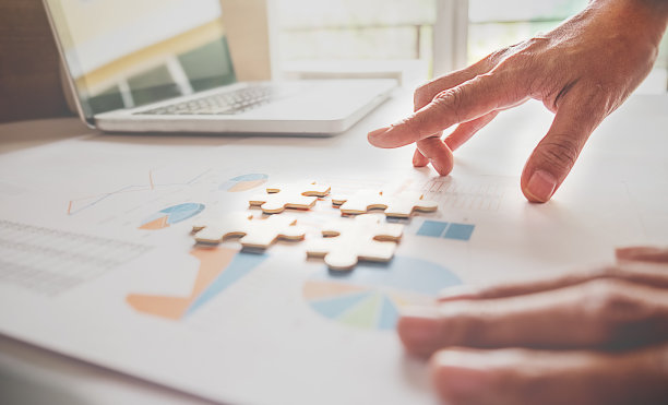 亚洲商务女性手在一个木制办公桌上挑拼图。商业解决方案，成功和战略概念。商人手接拼图。近距离的照片与选择焦点。图片下载