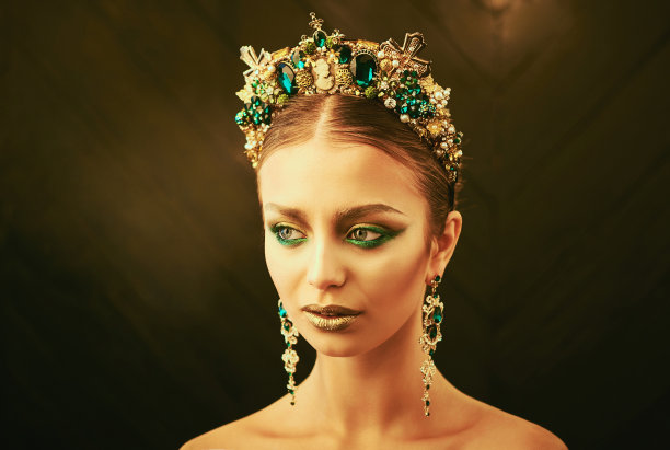 美丽的脸。漂亮的黑发女孩戴着金色的皇冠，戴着耳环，晚装上了职业装。图片下载
