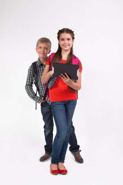 女生站在一个白色的背景与一个背包和平板电脑在手里，从她的学生的目光兴趣看平板电脑图片下载